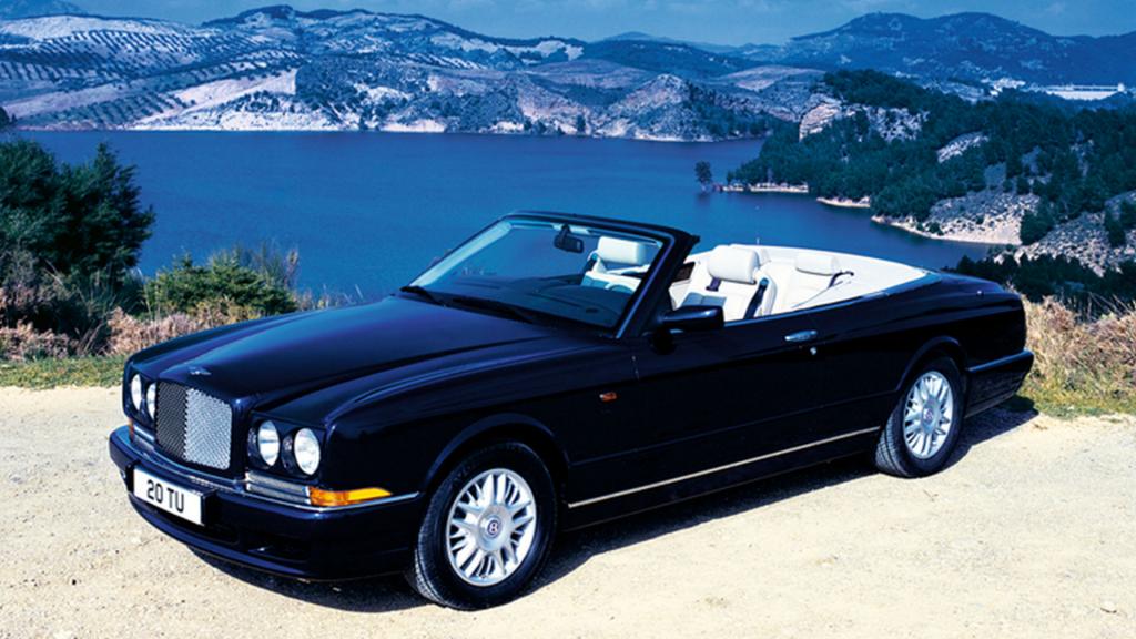 Bentley Azure, roof down, parked on a hill with water body in background.