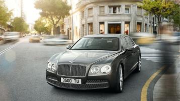 Bentley Flying Spur Mulliner, front side view with duo tone, exterior and matrix grille with black surround, driving on road.