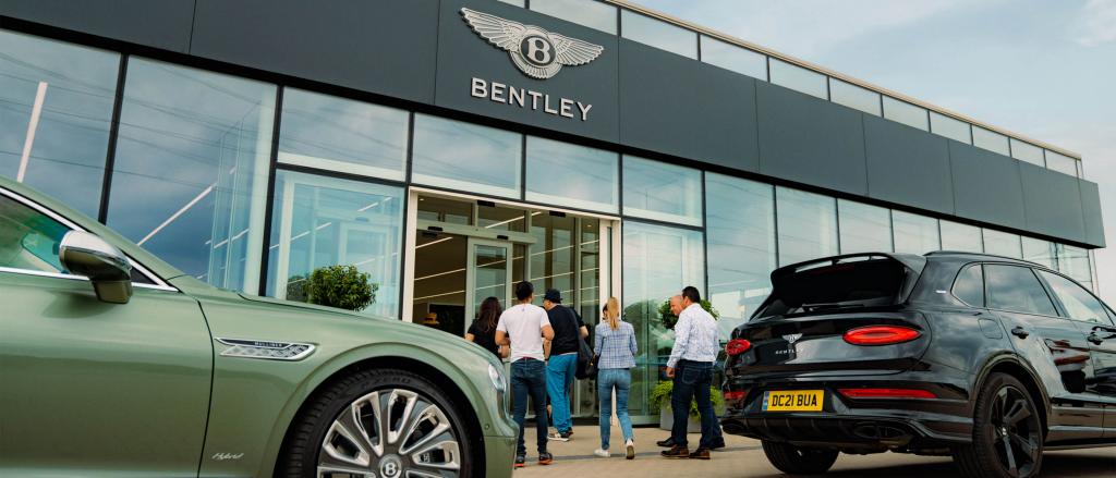 Six visitors entering Bentley CW 1 house in glass exterior, with rear view of Bentley Bentayga in Beluga colour