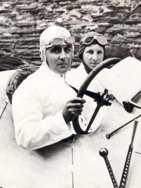 Walter Owen Bentley, on driver' seat of Bentley race car with steering wheel and a passenger in view.