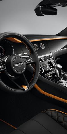 Driver side view of Bentley Continental GT Speed with steering wheel in view featuring High Gloss Carbon Fibre veneer and Mandarin by Mulliner hide contrasted by Beluga hide. 