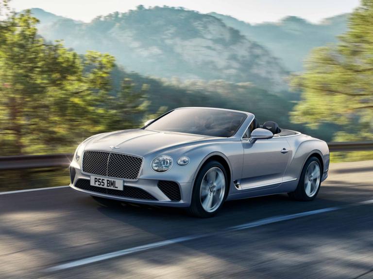 Bentley Continental GTC Signature model in Moonbeam colour featuring Black gloss matrix grille with chrome surround, driving with greenery in backdrop.