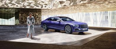 A lady / women / model / person posing infront of Bentley Flying Spur Mulliner W 12 in Tanzanite Purple, side angled view featuring 22 inch Mulliner Wheel Painted and Polished.
