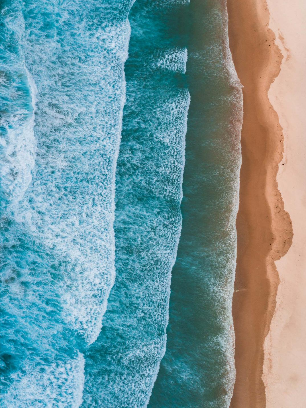 Birds eye view of waves hitting sandy shoreline.