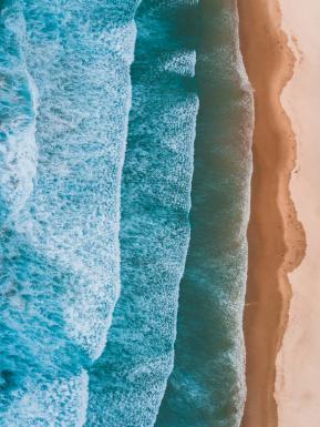 Birds eye view of waves hitting sandy shoreline.