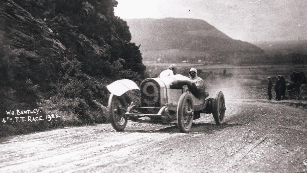 Bentley 3 Litre race car, on an unpaved race track with mountains in backdrop.