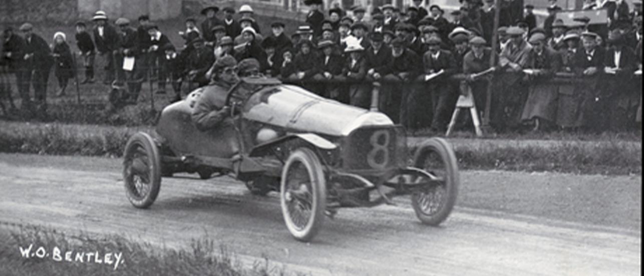 Legendary Bentley DFP driving along a racetrack with spectators in the background