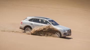 Bentley Bentayga, side angled view effortlessly driving in sand, featuring 22 inch alloy wheels and fluted front grille.