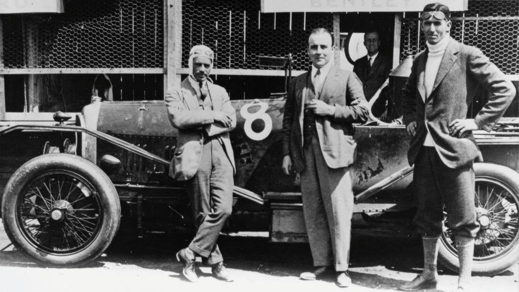 Side view of Bentley Speed Six and Walter Owen posing with it and trees in backdrop.