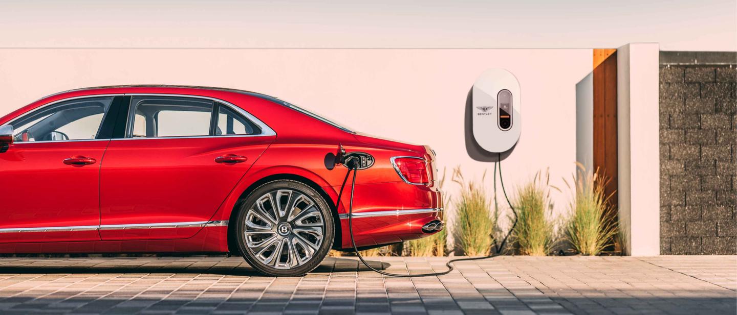 Side view of Bentley Flying Spur Hybrid in St.James Red (Solid) being recharged by Bentley branded PHEV home charger.