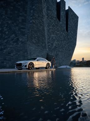 .Bentley Batur by Mulliner in [colour], side view featuring 22" 5 spoke directional alloy wheel – black painted with a female/person/ model posing at rear end.