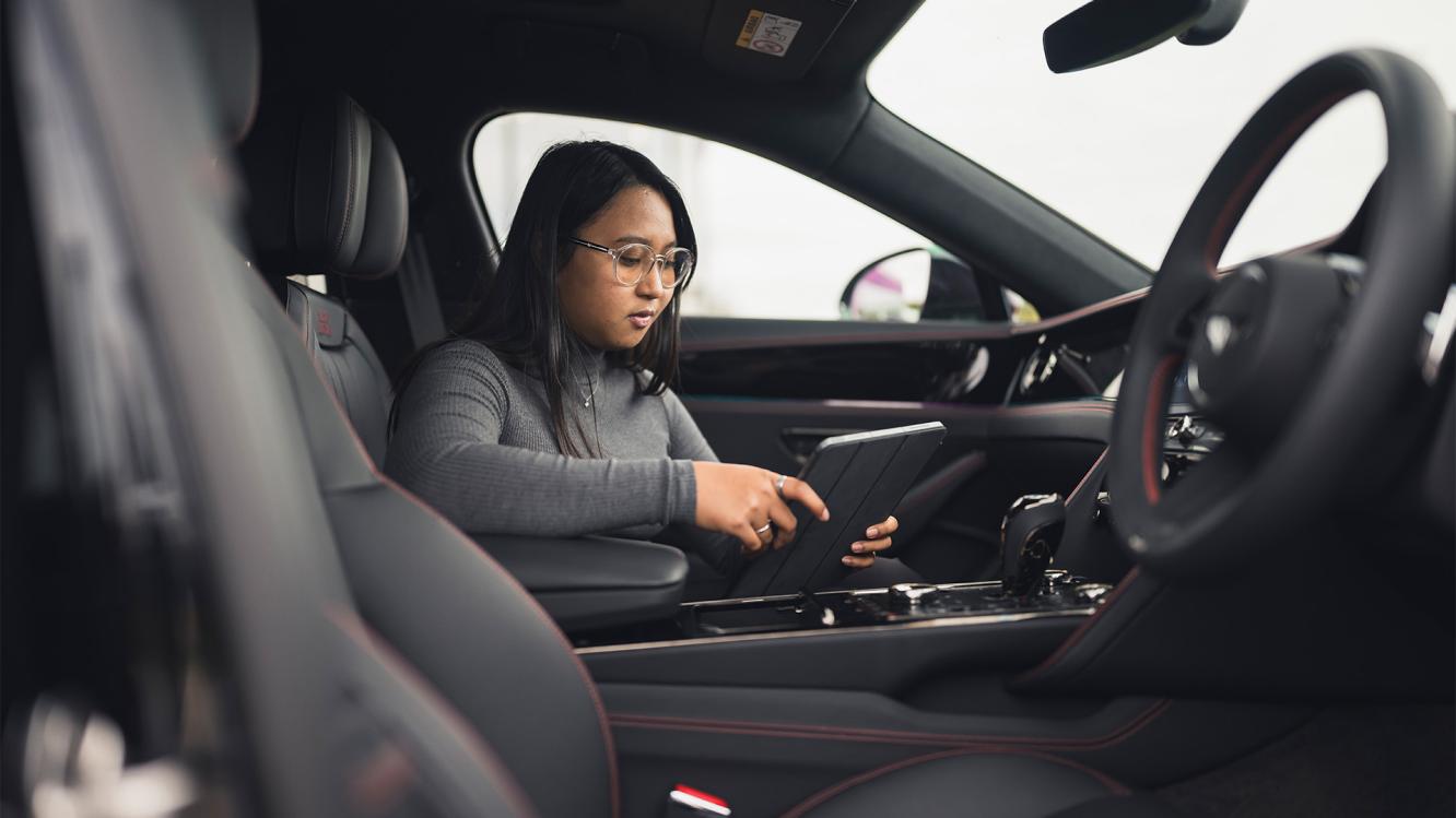 Yelena sat in the passenger seat of a Bentley, looking at an iPad.