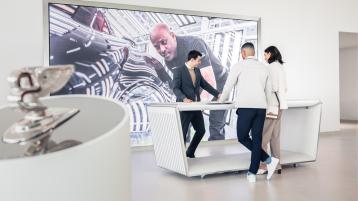 Bentley Factory tour, two visitors being met by friendly staff at reception and Flying B radiator mascot in view.