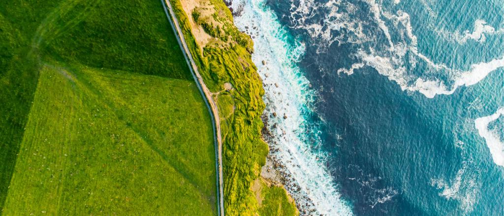 Birds eye view of a road dividing seaside on right and green pasture on left.