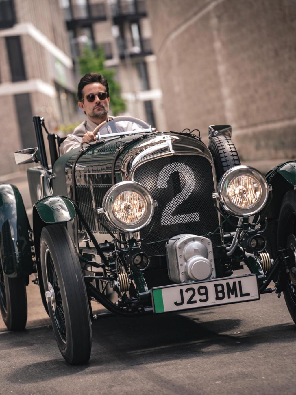 Man wearing sunglasses driving a Verdant green Bentley Blower.
