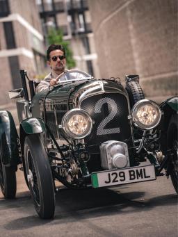 Man wearing sunglasses driving a Verdant green Bentley Blower.