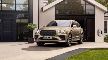 A Patina Bentayga Hybrid parked outside a home next to a Bentley wall charger
