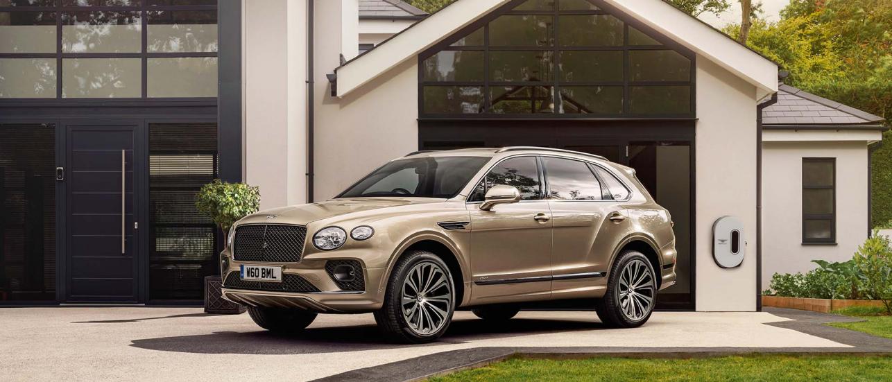 A Light Gazelle - by Mulliner coloured Bentley Bentayga Hybrid, side angled view featuring chrome matrix grille in black surround with Bentley branded EV charger in background.