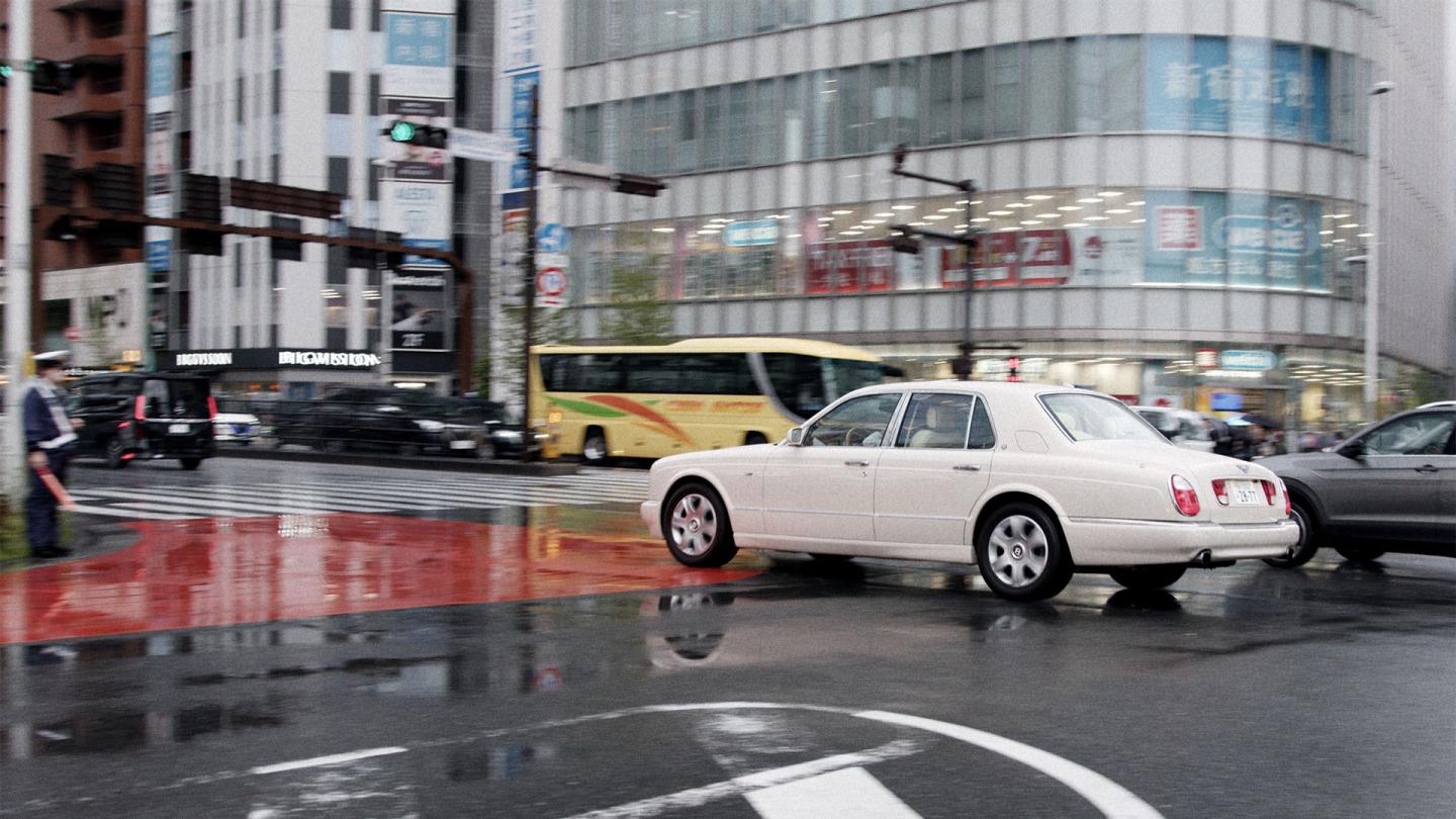 Exterior shot of Kota driving his Bentley Arnage.