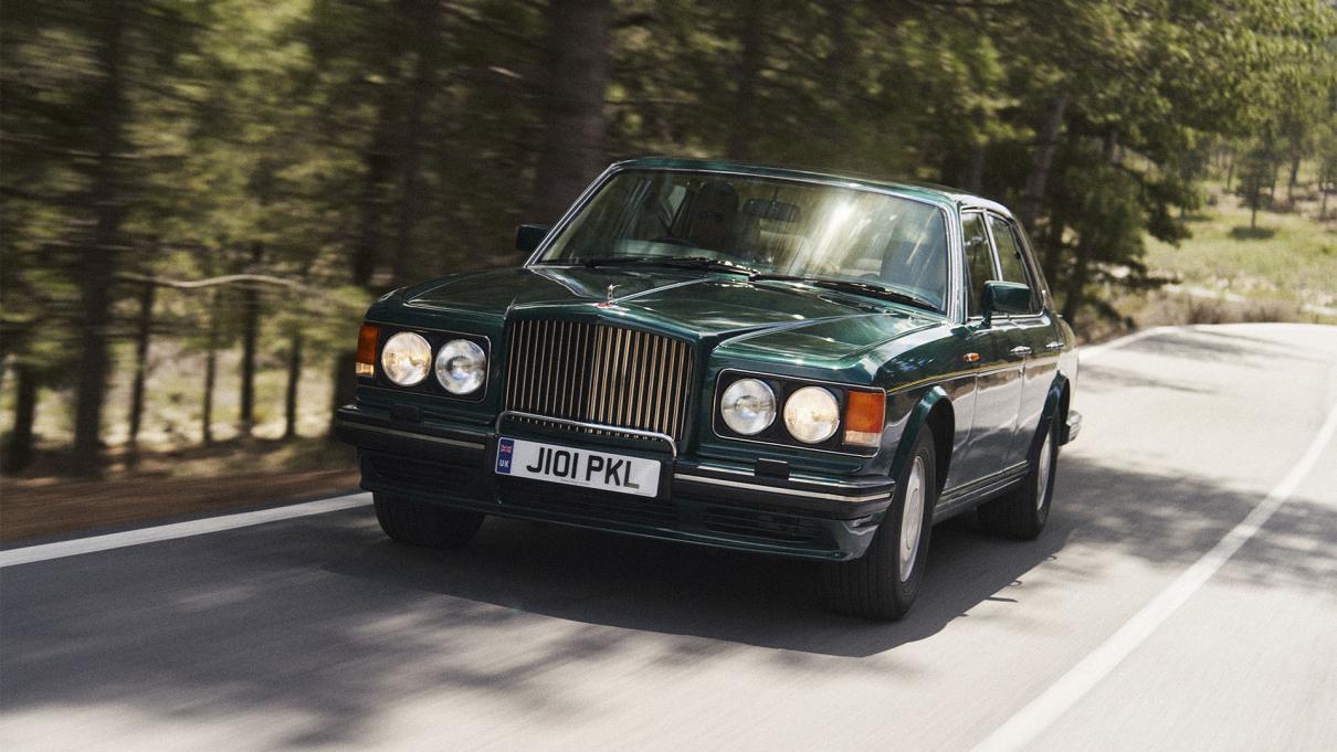 Bentley Turbo R driving along a tree lined road.