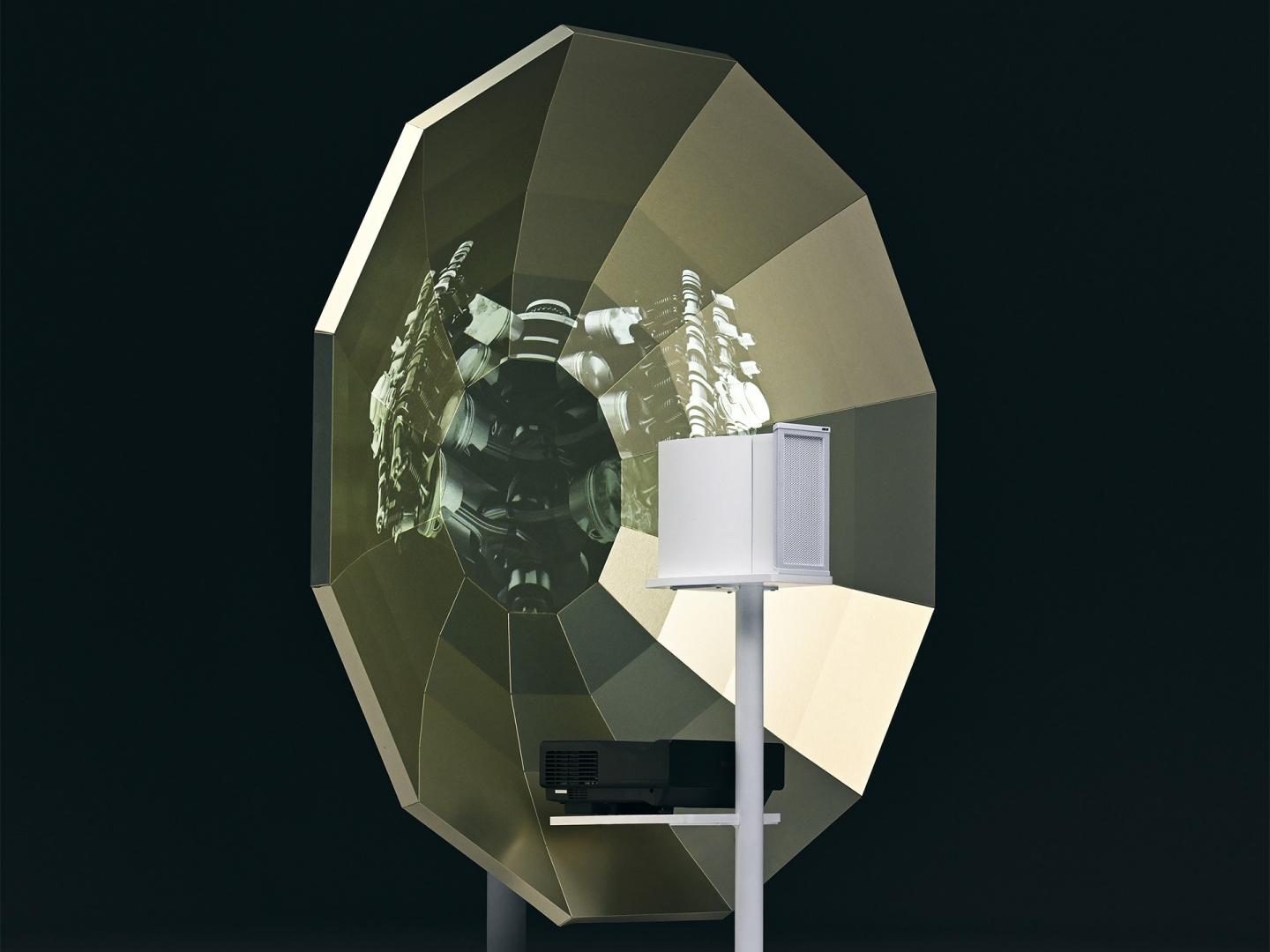Close up of the parabolic speaker with the image of a Bentley V8 engine projected onto it.