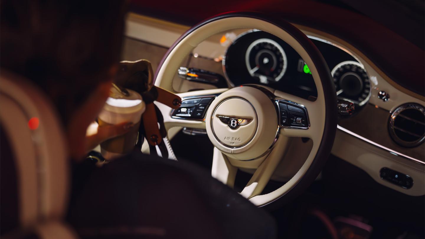 Person sat in a Bentley holding a coffee.