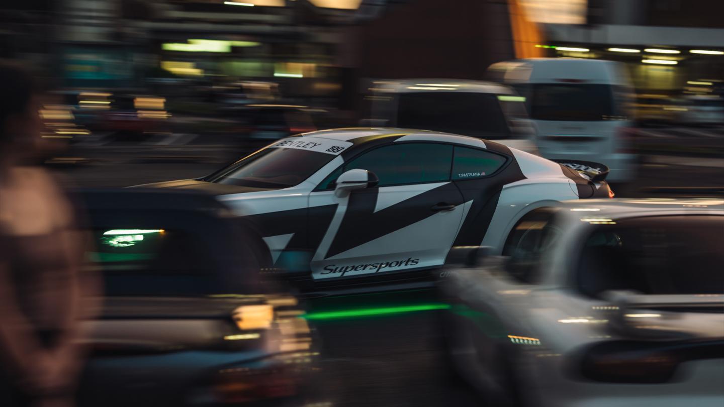 Bentley Supersports driving between rows of cars.