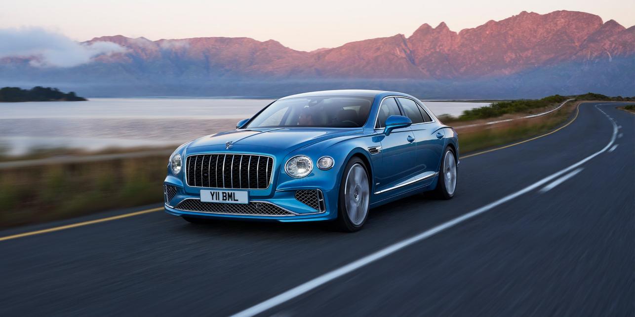 Front side angled view of Flying Spur Azure in Light Windsor Blue driving by the sea
