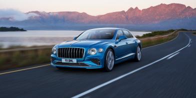 Front side angled view of Flying Spur Azure in Light Windsor Blue driving by the sea