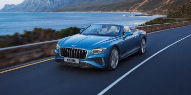 Front side angled view of Continental GTC Azure in Light Windsor Blue driving by the sea