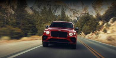 Front side view of Bentley Bentayga S  and matt black matrix grille, driving on road with mountains in view.