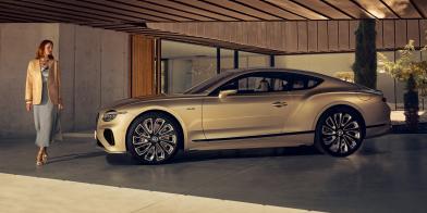 Side Profile of the new hybrid Continental GT Mulliner in Patina parked in front of a house with a model walking beside it