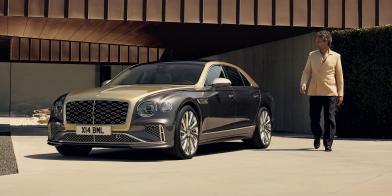 Front three quarter of the new hybrid Flying Spur Mulliner parked in front of a house with a model walking beside it