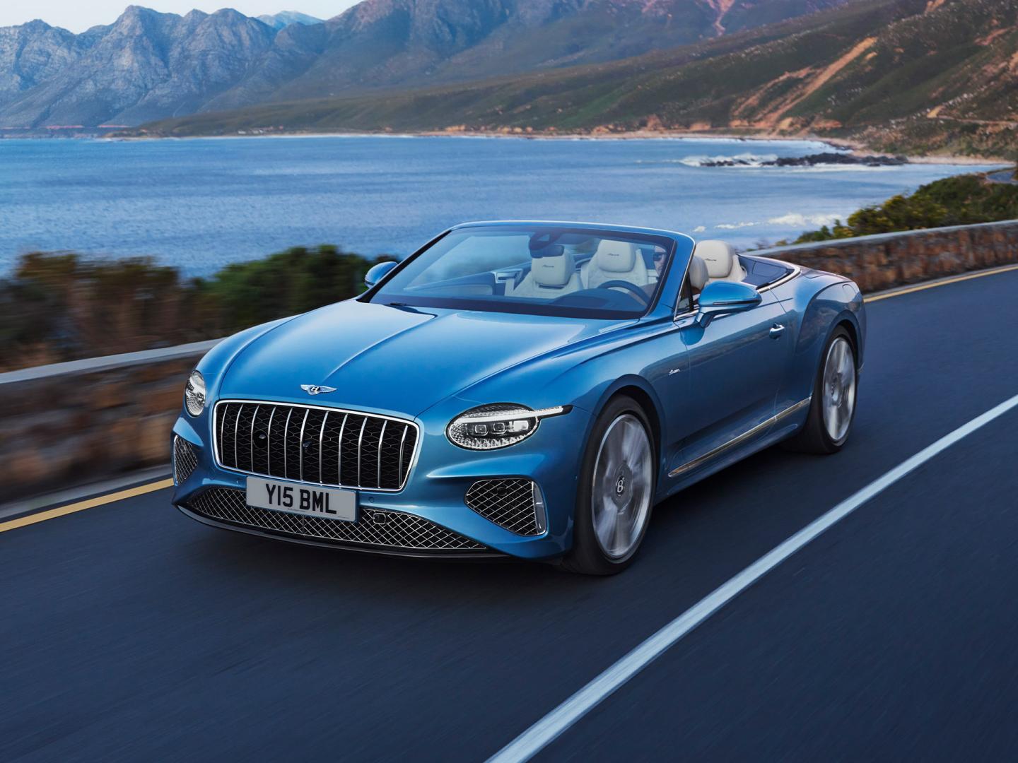 Front side angled view of Continental GTC Azure in Light Windsor Blue driving by the sea