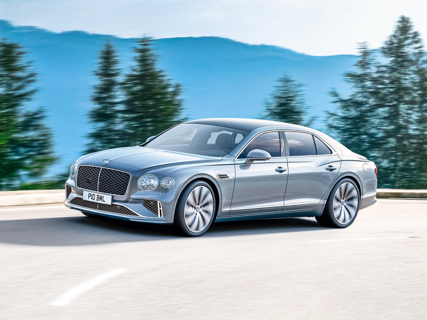 Bentley Flying Spur Signature model, in Moonbeam exterior colour featuing 21 inch Ten Twin Spoke - Painted wheels, diving on road with trees in backdrop.