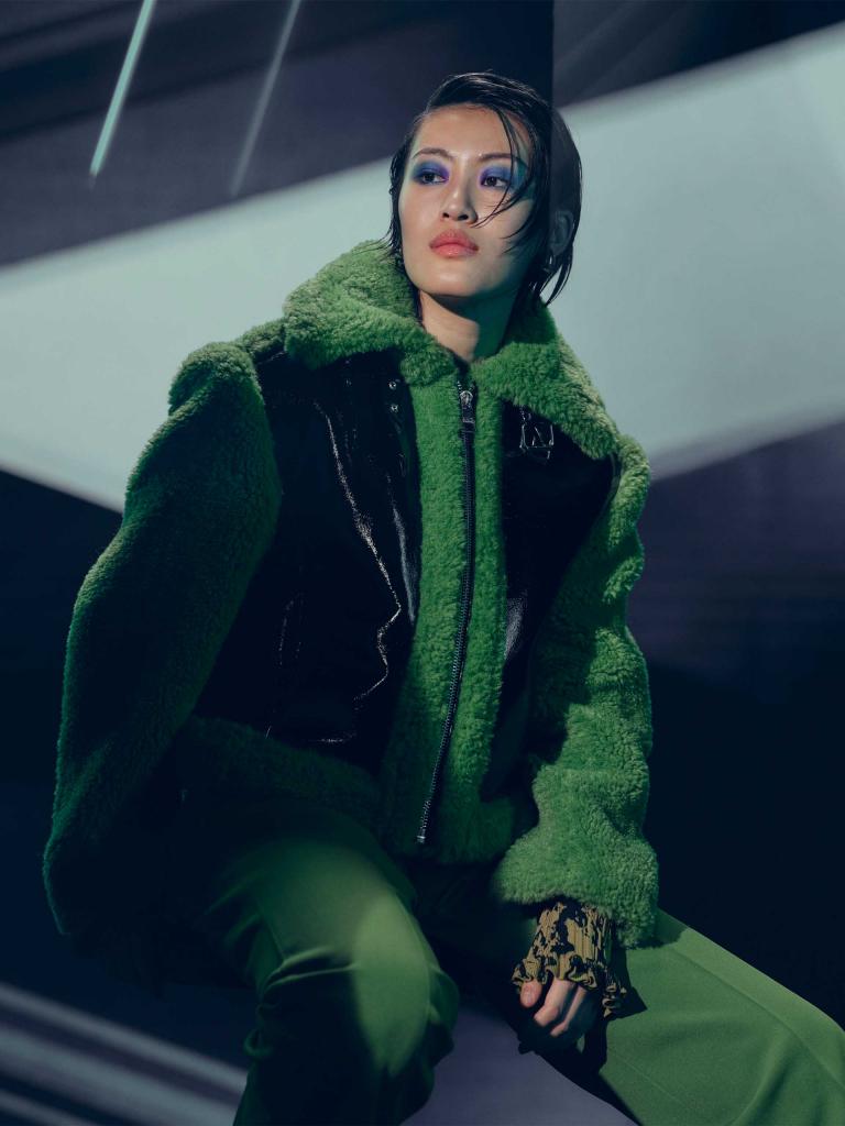 Individual/Woman/Lady dressed in green and black coloured jacket posing for a picture.