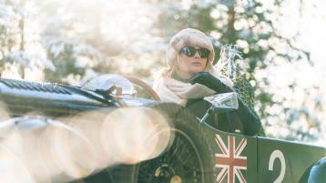 Close up view of a driver wearing wind protective goggles, driving a Bentley Blower Jnr 