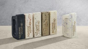 Six abstract patterned trophies made from London Clay featuring Dezeen awards engraving, placed on marble surface. 