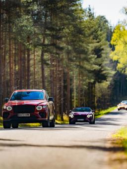 Front view Bentley Bentaya and Bentley Continental GT in St James red, driving along a green road.