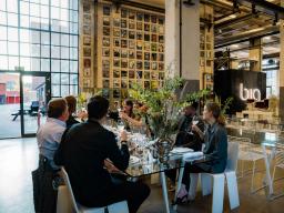 Group of people seated on a glass dining table and raising a toast.