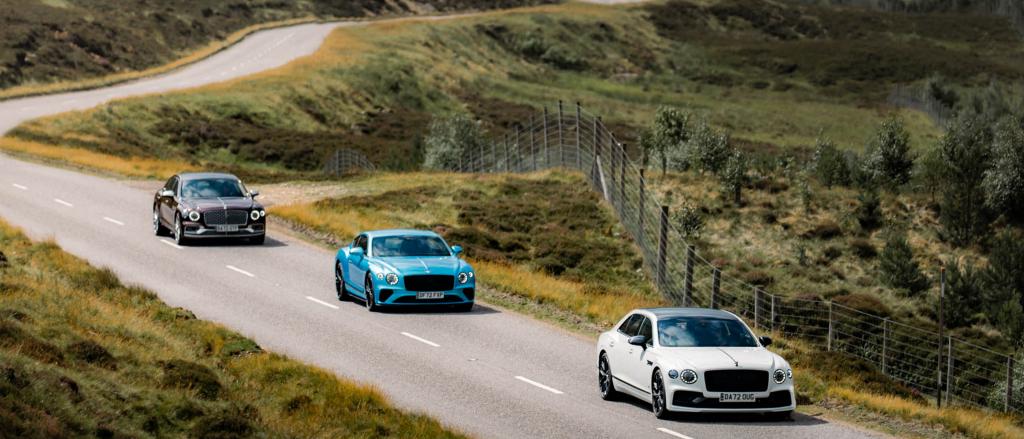 Bentley Flying Spur in Snow Quartz colour driving ahead of Bentley Continental GT and Bentley Flying Spur Mulliner, with country side in Backdrop. 