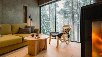 Room overlooking trees covered in snow through large window. 