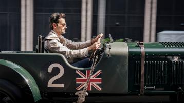 Side view of Bentley Blower JNR in Verdant green being driven in urban setting with driver in view.