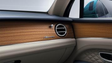 Interior passenger side view of Bentley Bentayga EWB Azure, featuring Open Pore Koa veneer with Azure Overlays below Chrome metal bulls-eye air vents.  
