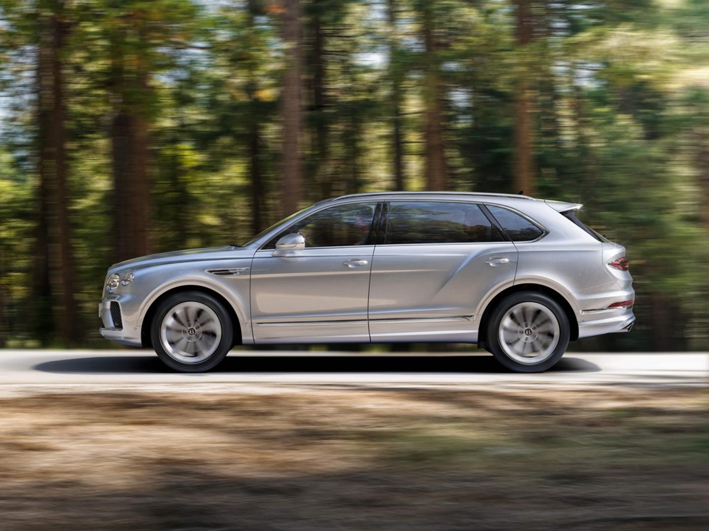 Side view of Bentley Bentayga EWB in Moonbeam colour driving through forest featuring Bentley ‘B’ wing vent.