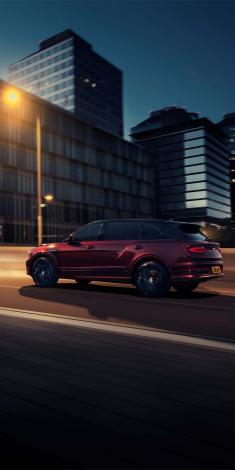 Bentley Bentayga EWB Mulliner with Black Crystal over Cricket Ball exterior paint featuring 22 inch Mulliner Wheel - Black painted, driving in urban area.