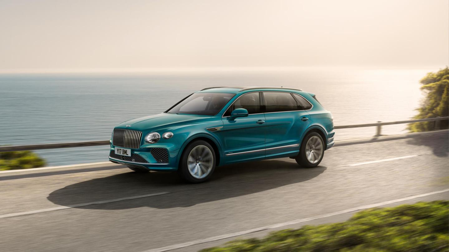 Front side angled view of Bentley Bentayga EWB Azure in Topaz Blue with chrome accent, driving along sea side.