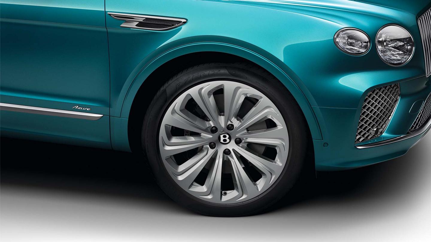  Side one quarter view of Bentley Bentayga Azure EWB in Topaz blue with chrome accents and Azure emblem in focus with 22 inch Ten Spoke Wheel.