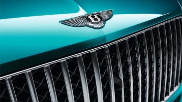 Close up view of a Topaz Blue coloured Bentley Bentayga Azure's polished chrome vertical-vaned front grille and Bentley front badge.