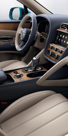 Passenger side view of Bentley Bentayga Azure overlooking a Heated, Duo Tone, 3 Spoke Hide Trimmed steering wheel and Open Pore Koa centre console.